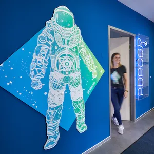 Eine Mitarbeiterin betritt den Eingangsbereich des Büros in Offenbach, an der Wand befinden sich ein großes Bild eines Astronauten in den Adacor-Farben und ein leuchtender „Adacor“ Schriftzug.