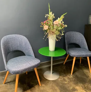 Eine Vase mit Blumen steht auf einem Tisch, daneben zwei Stühle.