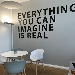 Stühle stehen um einen Tisch vor einer Wand mit der Aufschrift „Everything you can imagine is real“.
