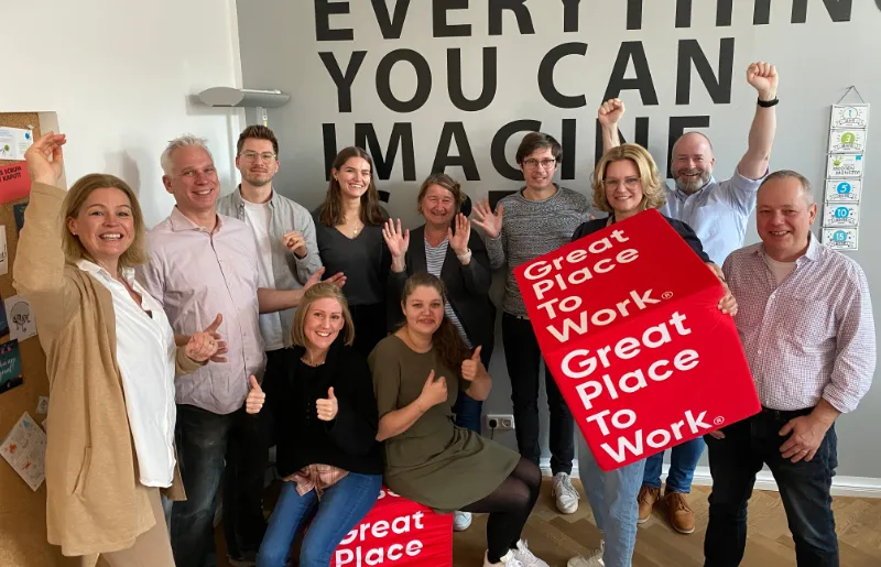 Mehrere Mitarbeiter lächeln in die Kamera und freuen sich über die „Great Place To Work“ Auszeichnung.