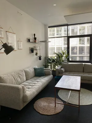 Blick in einen Meetingraum mit Sofas, einem Tisch, mehreren Pflanzen und Bildern an der Wand.