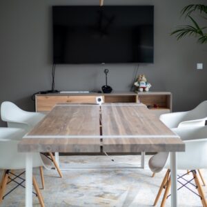 Ein Holztisch und Stühle stehen in einem Meetingraum, an der Wand hängt ein großer Bildschirm.